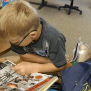 Kid reading a book with a Visions bag next to her