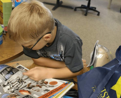 Kid reading a book with a Visions bag next to her