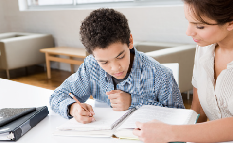 Young boy student of Visions In Education reviewing Home School Academy notes next to his mother while sitting in their home kitchen table