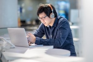 Asian male student working on online high school classes on laptop at library