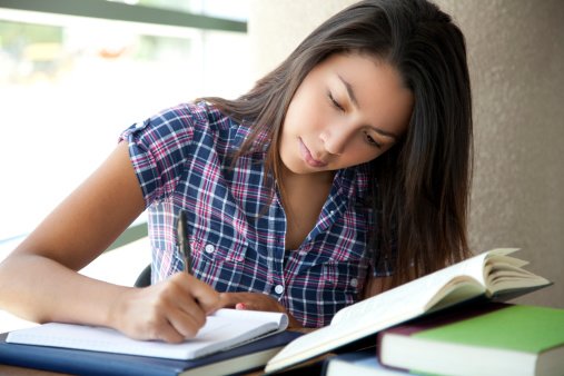A young hispanic female student of Visions In Education is doing her homework and writing on a notebook.