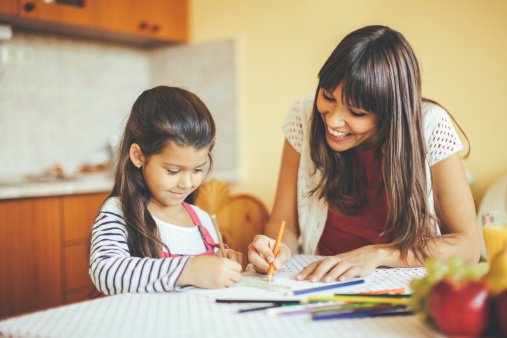 Mom and young daughter working through schoolwork together at home on kitchen table