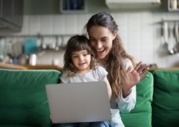 Happy mother and kid daughter waving hands looking at web camera using laptop for video call