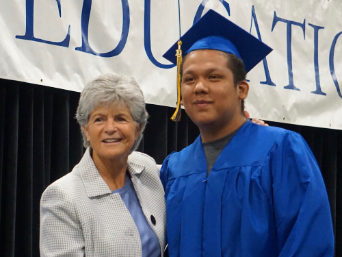 Summer grad posing on stage with Superintendent Jody Graf