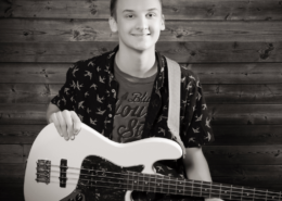 Male student smiling at the camera holding a guitar