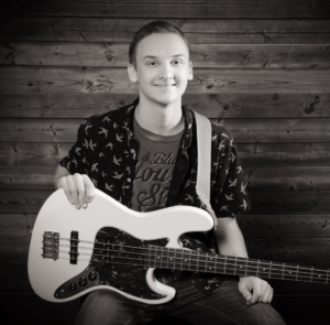 Male student smiling at the camera holding a guitar