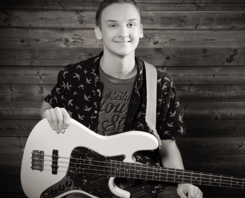 Male student smiling at the camera holding a guitar