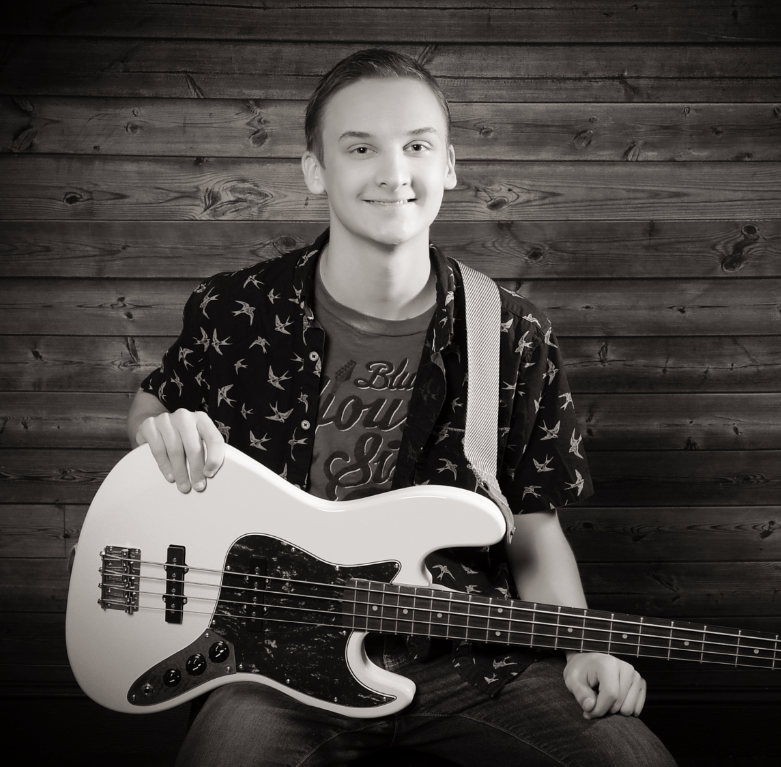 Male student smiling at the camera holding a guitar