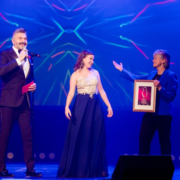 Women accepts award on stage with two presenters