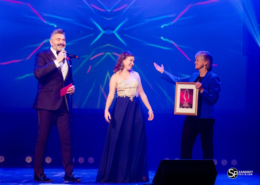 Women accepts award on stage with two presenters