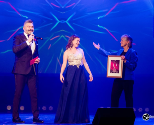 Women accepts award on stage with two presenters