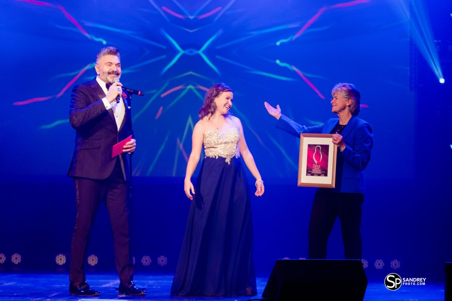 Women accepts award on stage with two presenters