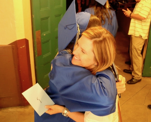 Grad in cap & gown hugging teacher