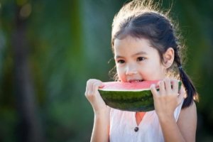 Cute asian little child girl eating watermelon fresh fruit in the garden