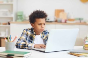 Portrait of teenage African boy using laptop while studying at home, remote education concept