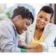 African American male student smiles while doing school work with teacher