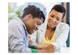 African American male student smiles while doing school work with teacher