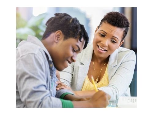 African American male student smiles while doing school work with teacher