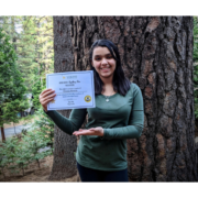 8th grader Elissa winner of 2020 spelling bee poses with certificate in front of large tree