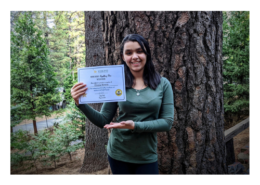 8th grader Elissa winner of 2020 spelling bee poses with certificate in front of large tree