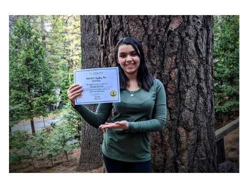 8th grader Elissa winner of 2020 spelling bee poses with certificate in front of large tree