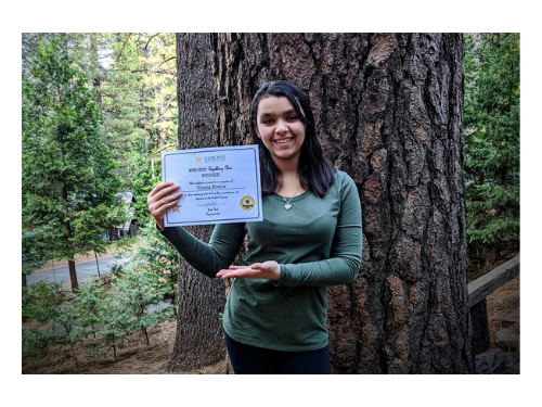 8th grader Elissa winner of 2020 spelling bee poses with certificate in front of large tree
