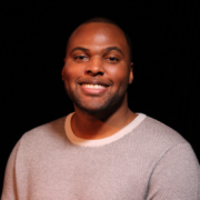 Male African American high school graduate smiles at the camera, black background