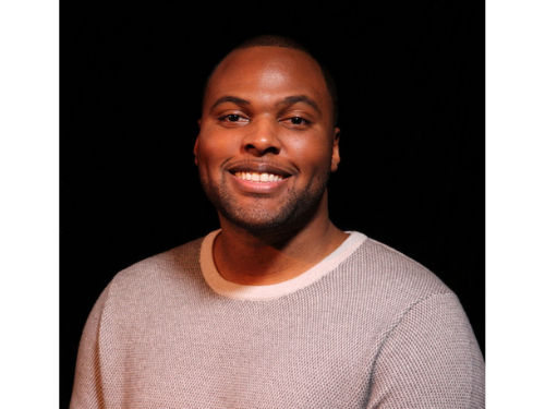 Male African American high school graduate smiles at the camera, black background