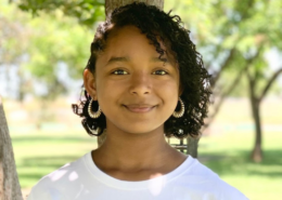 Mikaela, a teen student that owns her own business, smiles at the camera in a park