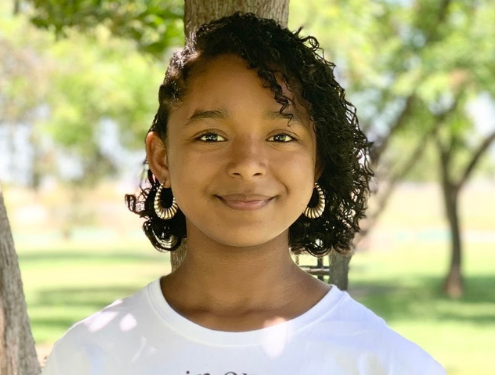 Mikaela, a teen student that owns her own business, smiles at the camera in a park