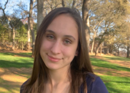 High school graduate smiles at the camera in a park