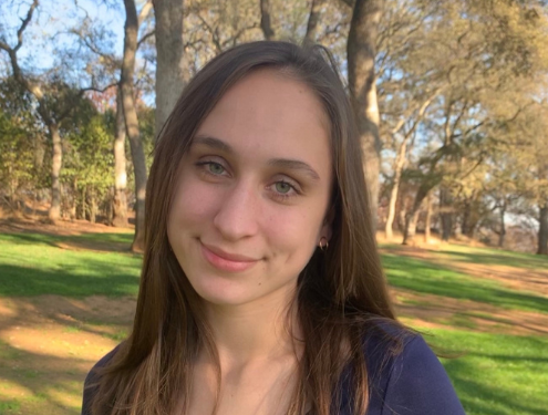 High school graduate smiles at the camera in a park