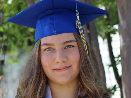 Marina smiles at the camera in blue graduation cap and gown; graduating from online high school