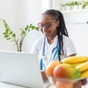 Smiling online high school student and aspiring nutritionist in her office, she is showing healthy vegetables and fruits, healthcare and diet concept.