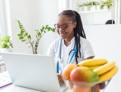 Smiling online high school student and aspiring nutritionist in her office, she is showing healthy vegetables and fruits, healthcare and diet concept.