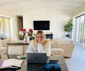 Blonde teen girl prepares for school education at home, sitting at kitchen counter with laptop