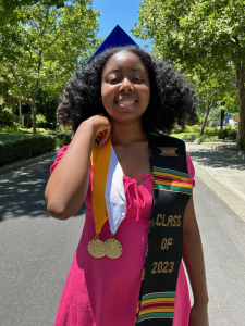 Black female graduate holds up her graduation medals wearing a pink dress before graduation