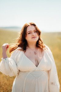 Redheaded high school female in a white dress poses in an open field for graduation pictures