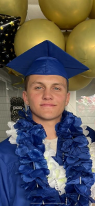 White male graduate in blue cap and flower leis in front of balloons before graduation
