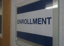 Blue and white sign with the word Enrollment on it on the wall at the Visions building