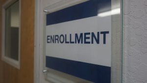 Blue and white sign with the word Enrollment on it on the wall at the Visions building