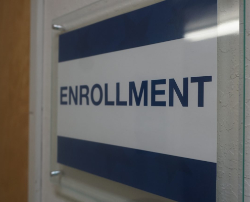 Blue and white sign with the word Enrollment on it on the wall at the Visions building