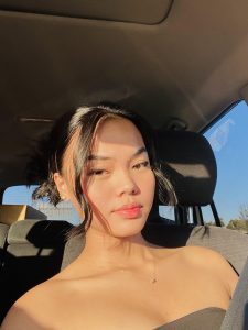 Asian female teen with hair pulled back takes selfie in a car