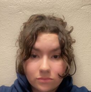 Female student with dark wavy hair standing in front of blank wall