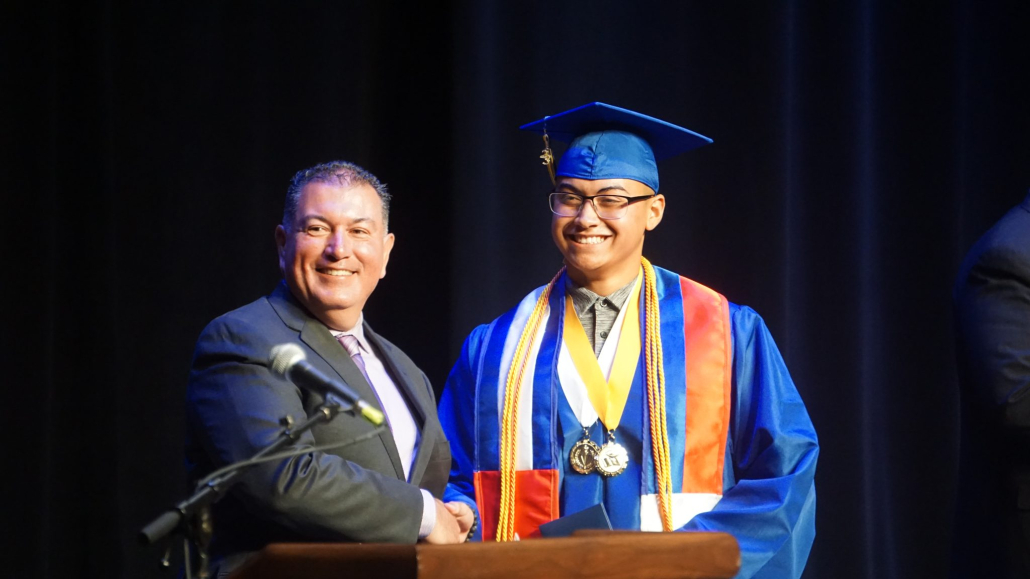 Male Superintendent poses with Filipino male graduate on staff at graduation