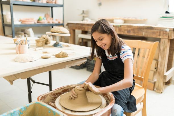 Happy preteen girl pursuing hobby of pottery while sitting in class