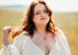 Redheaded high school female in a white dress poses in an open field for graduation pictures