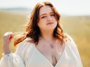 Redheaded high school female in a white dress poses in an open field for graduation pictures