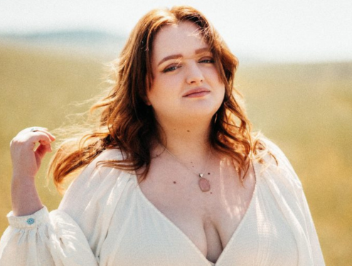 Redheaded high school female in a white dress poses in an open field for graduation pictures