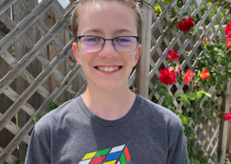 High school student smiles for his photo wearing glasses and a shirt with a Rubik's Cube on it